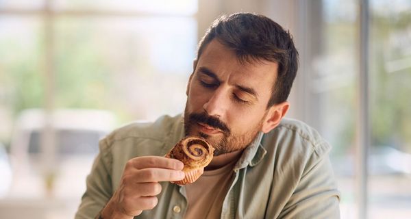 Mann riecht mit geschlossenen Augen an einem Zimtwirbel-Muffin.