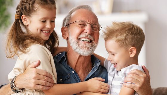 Älterer Mann lacht mit zwei lachenden Kindern in den Armen. 