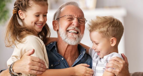 Älterer Mann lacht mit zwei lachenden Kindern in den Armen. 