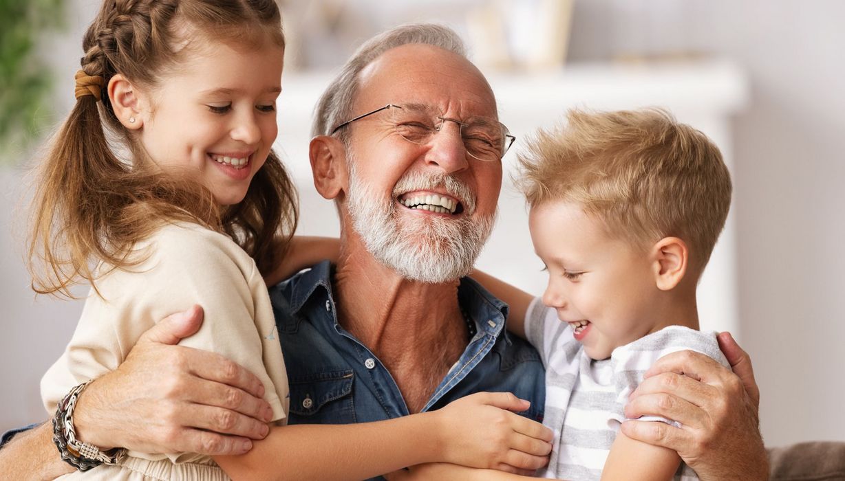 Älterer Mann lacht mit zwei lachenden Kindern in den Armen. 