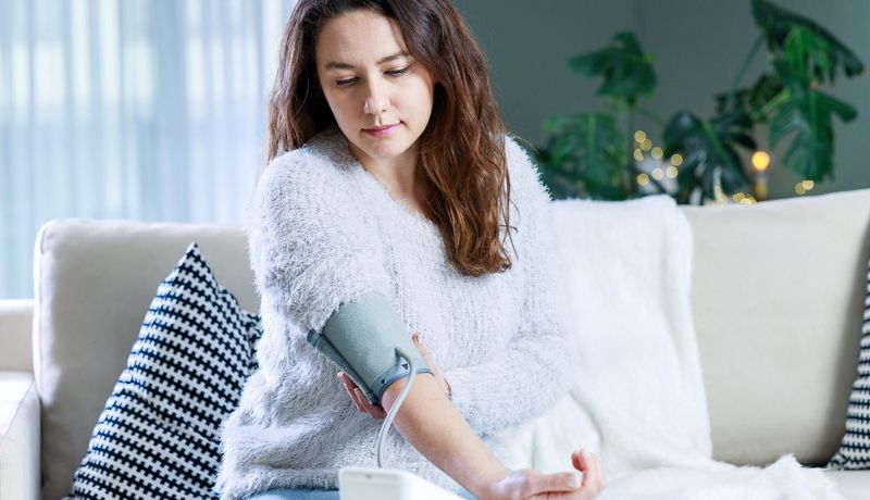 Junge Frau legt sich die Manschette zum Blutdruckmessen an.