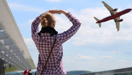 Szene vor Flughafen, Frau von hinten, Karohemd, Jeans, beobachtet Flugzeug beim Abflug