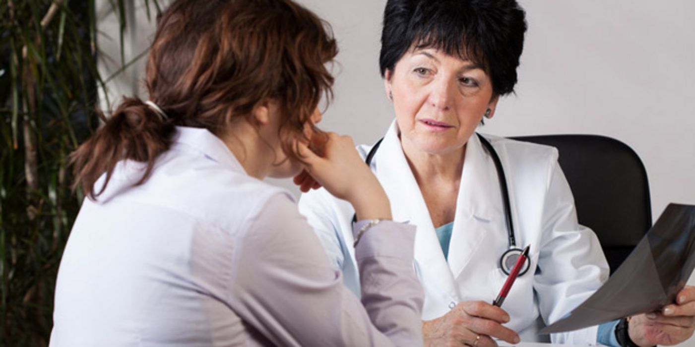 Ärztin um die 60 im ernsten Gespräch mit Patientin (Rückenansicht)