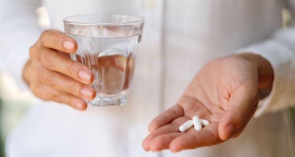 Frau, hält ein Glas Wasser und zwei Tabletten in der HAnd.