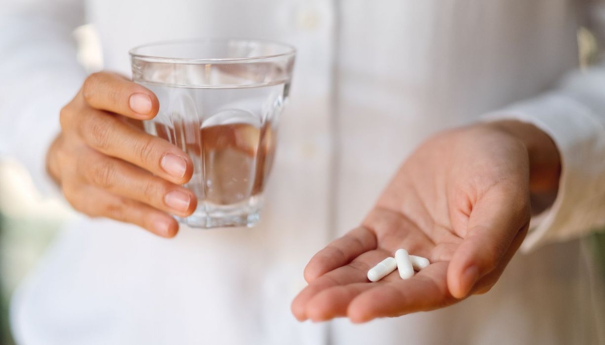 Frau, hält ein Glas Wasser und zwei Tabletten in der HAnd.