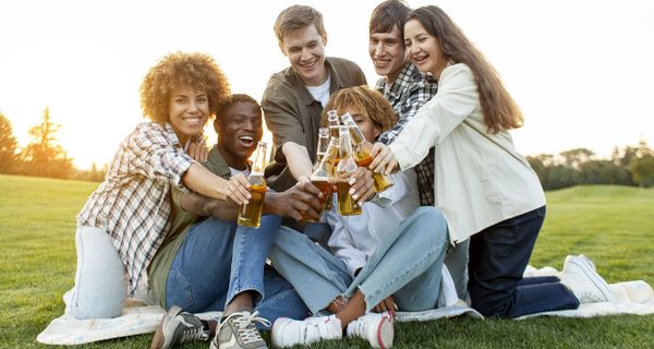 Eine Gruppe Jugendlicher trifft sich im Park und mit stößt mit Bier in Glasflaschen an.