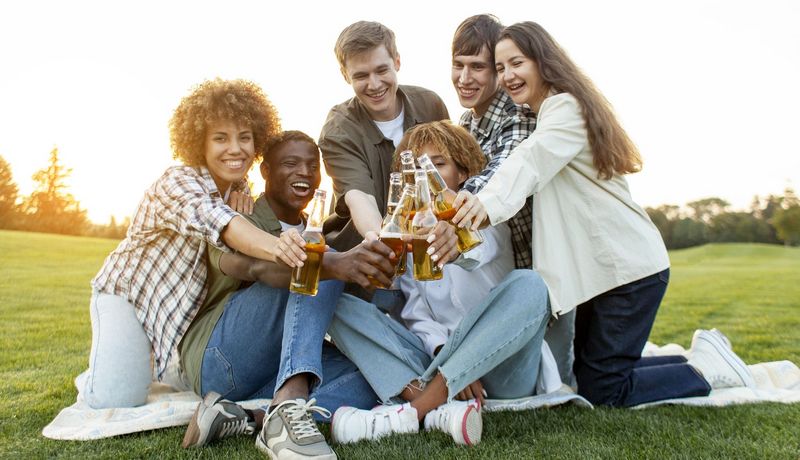 Eine Gruppe Jugendlicher trifft sich im Park und mit stößt mit Bier in Glasflaschen an.