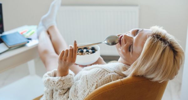 Junge Frau sitzt auch Sessel und hält einen Löffel und ein Müsli in den Händen.