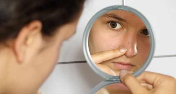 Junge Frau betrachtet im Spiegel einen Pickel auf der Nase
