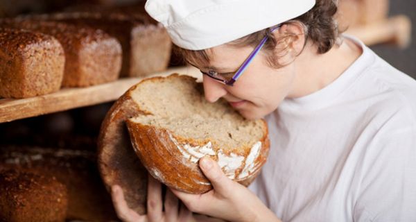 Jüngerer Bäcker hat ein Brot auseinandergebrochen und riecht genüsslich am Teig 