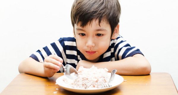 Kleiner Junge sitzt vor einem Teller mit Reis mit einem Löffel in der Hand.