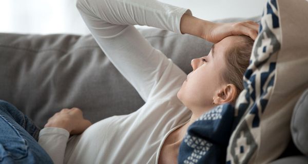 Junge Frau, liegt auf der Couch, erschöpft.