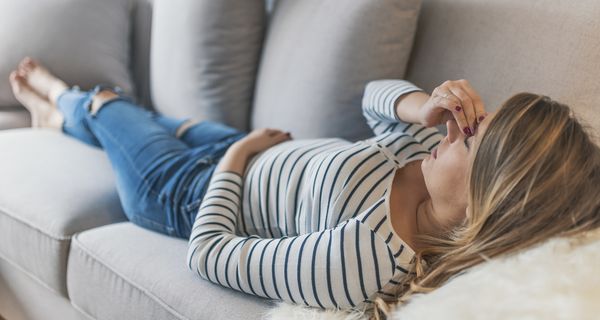 Junge Frau, liegt auf der Couch und hält eine Hand an ihre Schläfe.