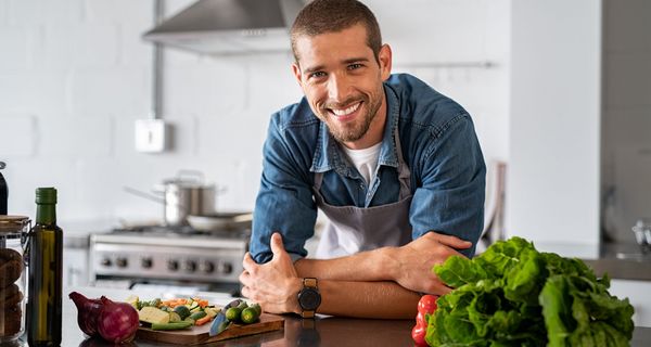 Lächelnder junger Mann beugt sich über eine Küchenarbeitsplatte.