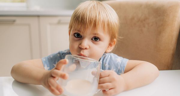 Kleinkind, etwa 2 Jahre alt, hält ein großes Glas Milch in den Händen. Es blickt fragend.