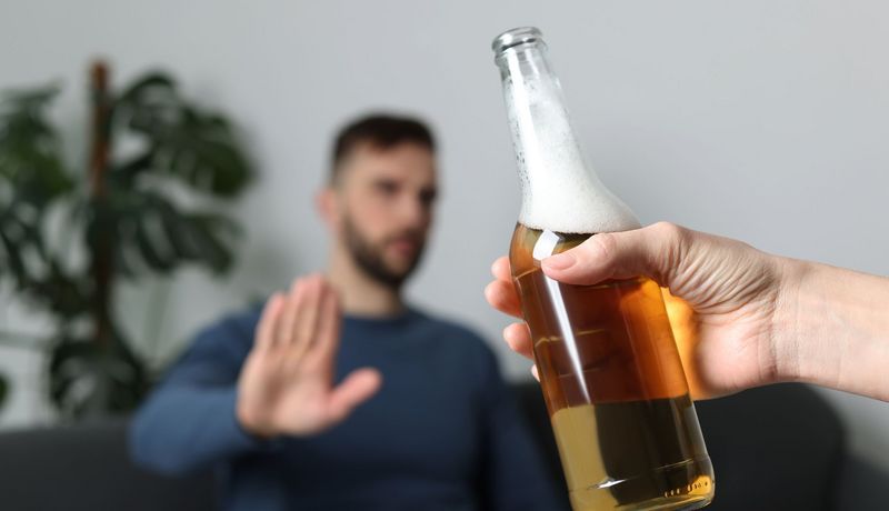 Mann sitzt auf Sofa un lehnt mit der Hand ein ihm angebotenes Bier ab.