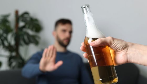 Mann sitzt auf Sofa un lehnt mit der Hand ein ihm angebotenes Bier ab.
