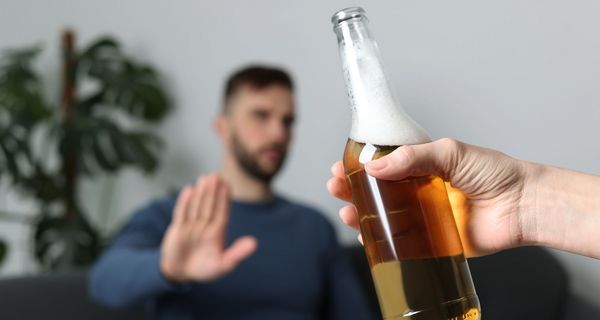 Mann sitzt auf Sofa un lehnt mit der Hand ein ihm angebotenes Bier ab.