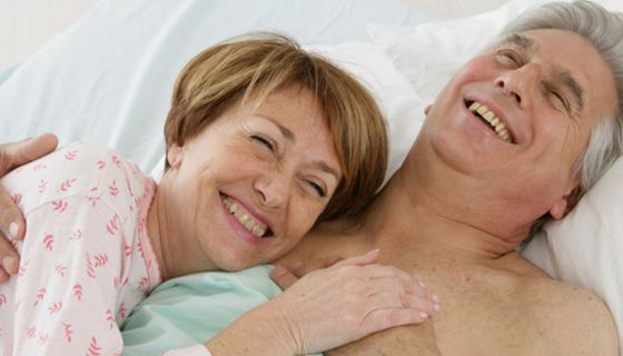 Älteres Paar im Bett; Frau schmiegt sich an Mann