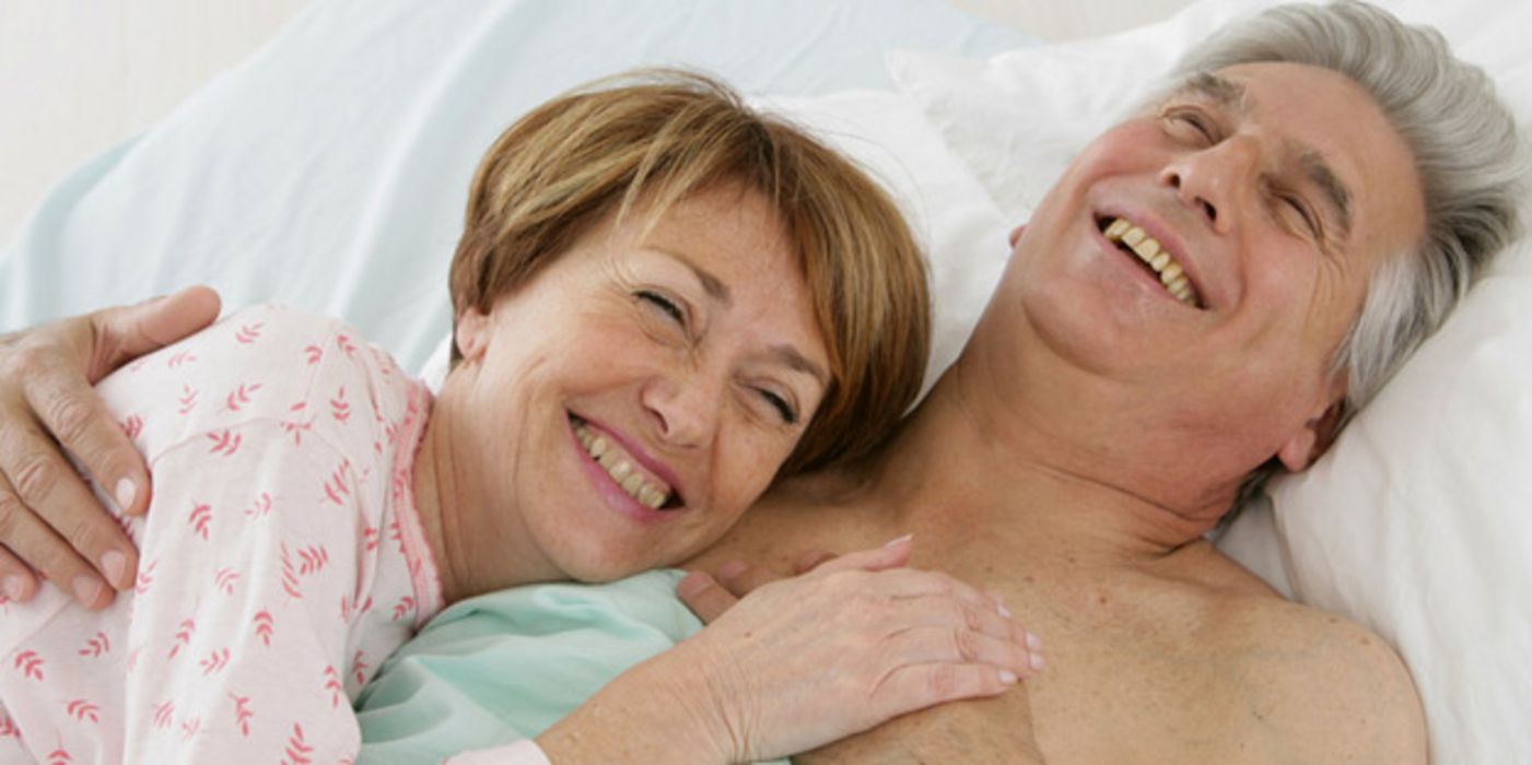 Älteres Paar im Bett; Frau schmiegt sich an Mann