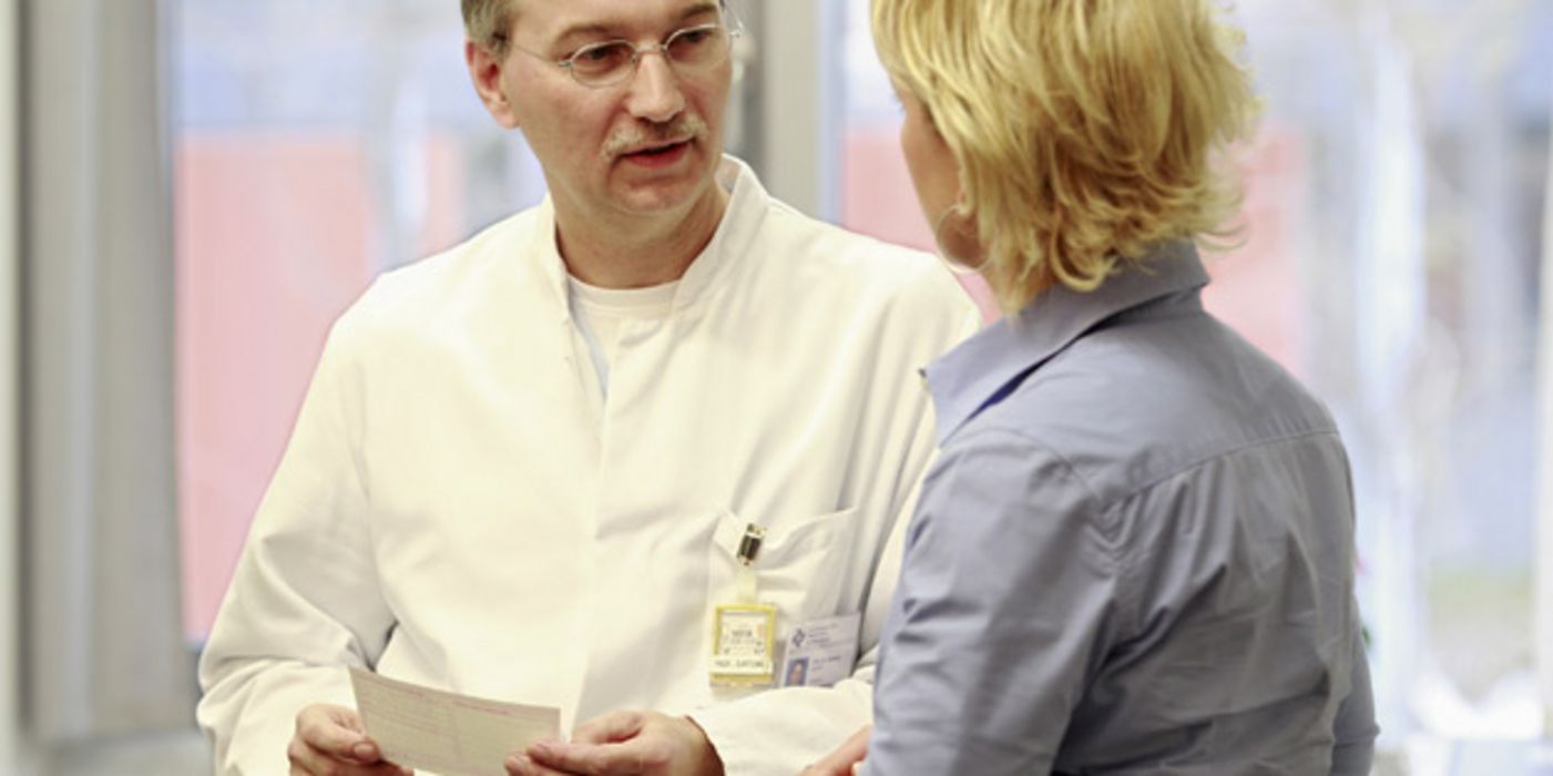 Arzt im Gespräch mit einer Patientin, in der Hand hält er ein Rezept