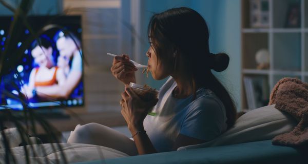 Frau sitzt im Dunkeln vor dem Fernseher und isst.