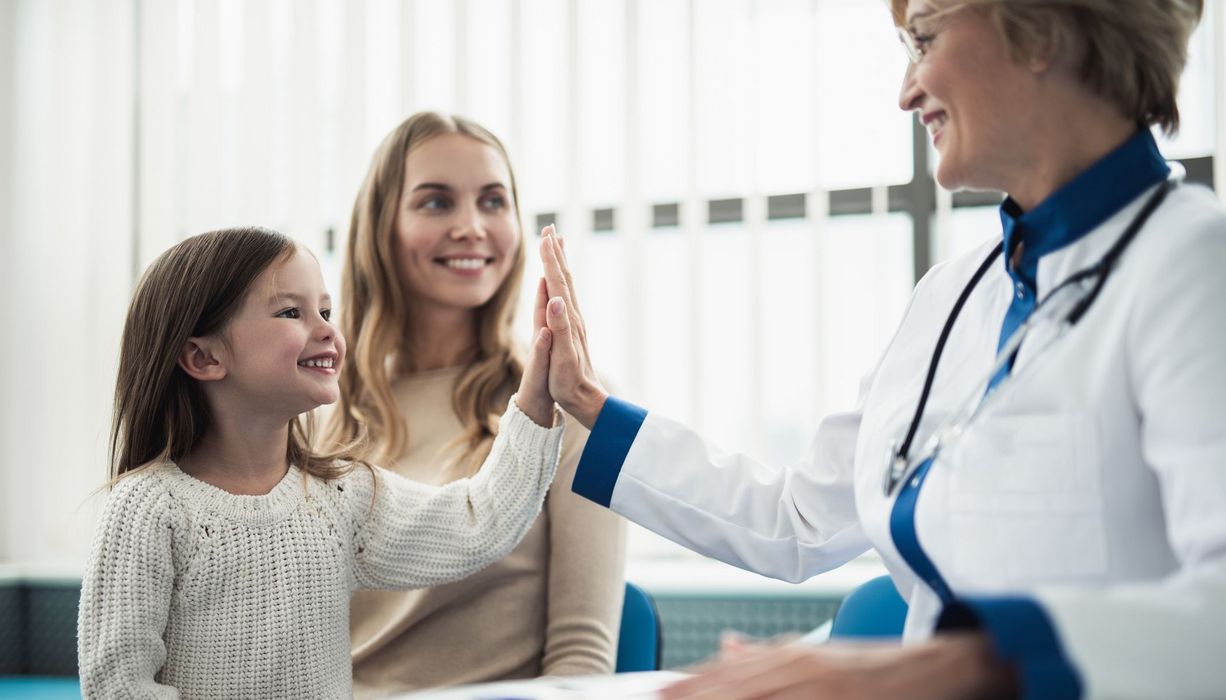 Mutter und Tochter bei Kinderärztin, Kind gibt Ärztin "High Five"