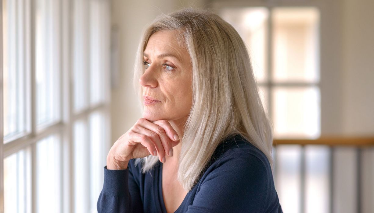 Blonde Frau 50+ blickt aus dem Fenster.