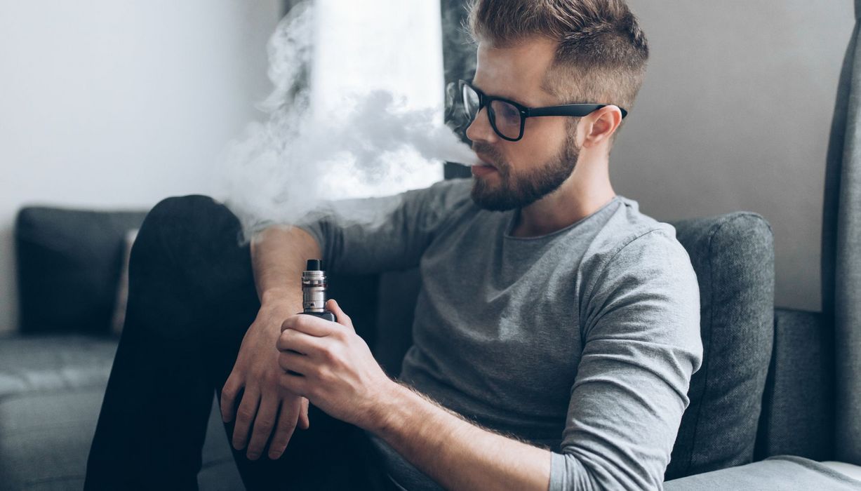 Junger Mann mit Brille raucht mittels E-Zigarette.