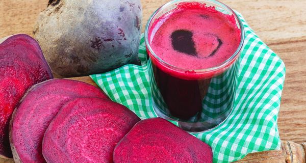 Ein Glas voller Rote Bete-Saft steht neben einer aufgeschnittenen Rote Bete-Knolle.