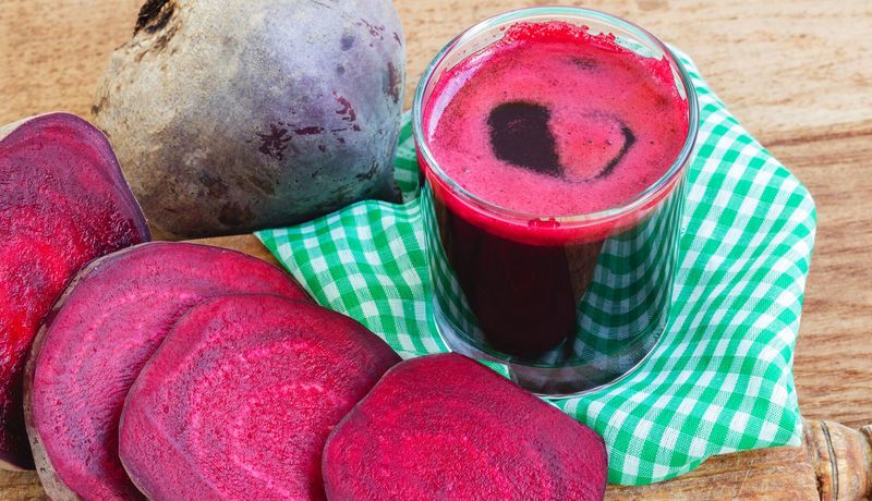 Ein Glas voller Rote Bete-Saft steht neben einer aufgeschnittenen Rote Bete-Knolle.