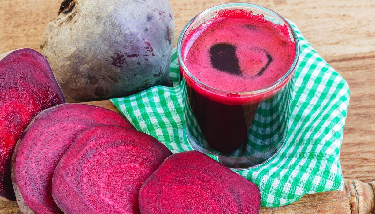 Ein Glas voller Rote Bete-Saft steht neben einer aufgeschnittenen Rote Bete-Knolle.