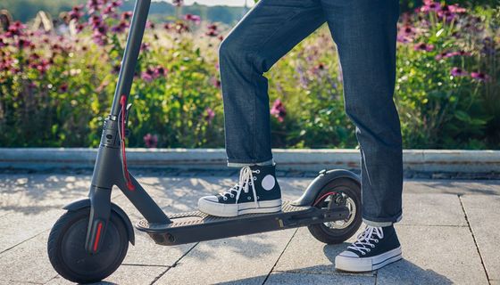 Ein junger Mensch steht mit einem Fuß auf einem E-Roller.