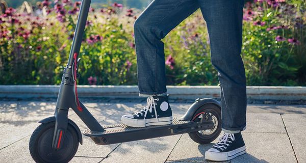 Ein junger Mensch steht mit einem Fuß auf einem E-Roller.