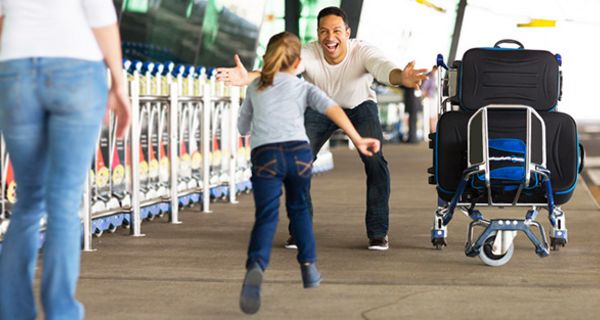 Mann wird am Flughafen stürmisch von junger Tochter begrüßt, die in seine ausgebreiteten Arme läuft; Mutter mit dem Rücken zur Kamera am linken Bildrand