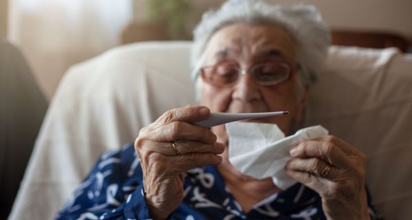 Ältere Frau, ca. 80 Jahre alt, schaut auf Fieberthermometer.