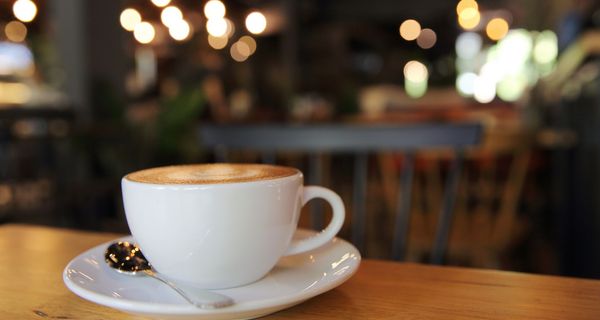 Tasse Kaffee, im Hintergrund ein Café mit Lichtern.