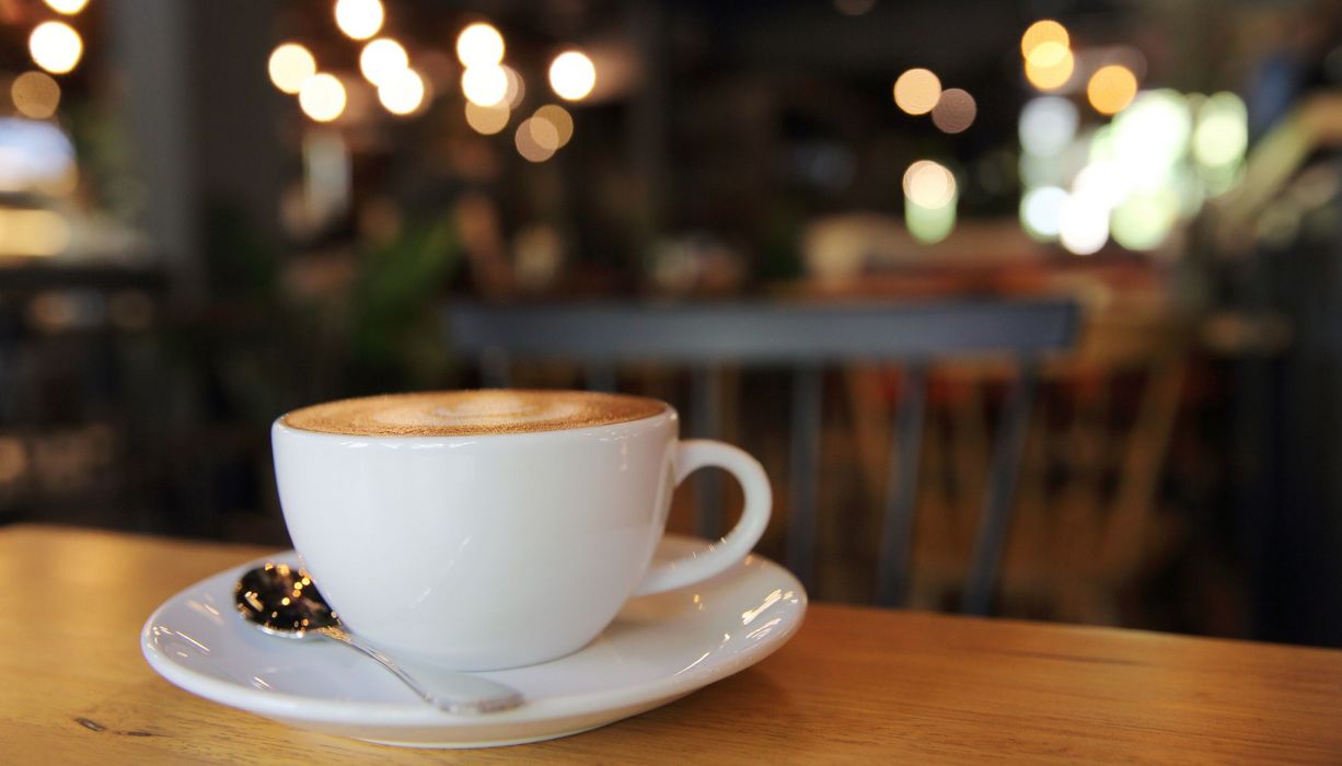 Tasse Kaffee, im Hintergrund ein Café mit Lichtern.