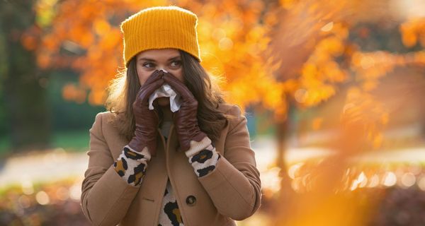 Frau schnäuzt sich die Nase in herbstlicher Natur.