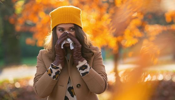 Frau schnäuzt sich die Nase in herbstlicher Natur.