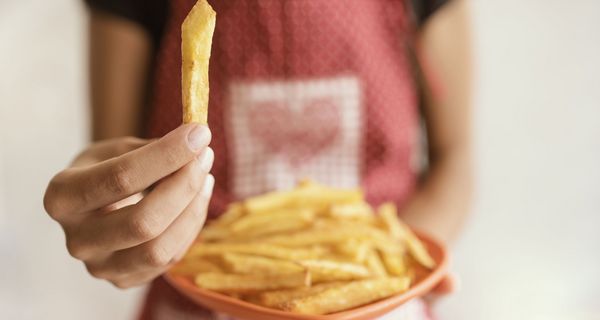 Frau mit einem Teller Pommes, hält eine Pommes in die Kamera.