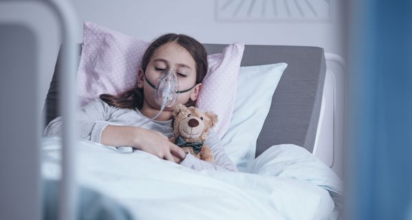 Kind liegt mit Atemmaske und Teddybär im Krankenhausbett