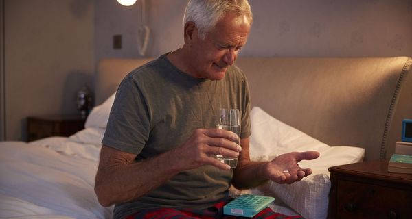 Älterer Mann, sitzt auf dem Bett und nimmt Tabletten.