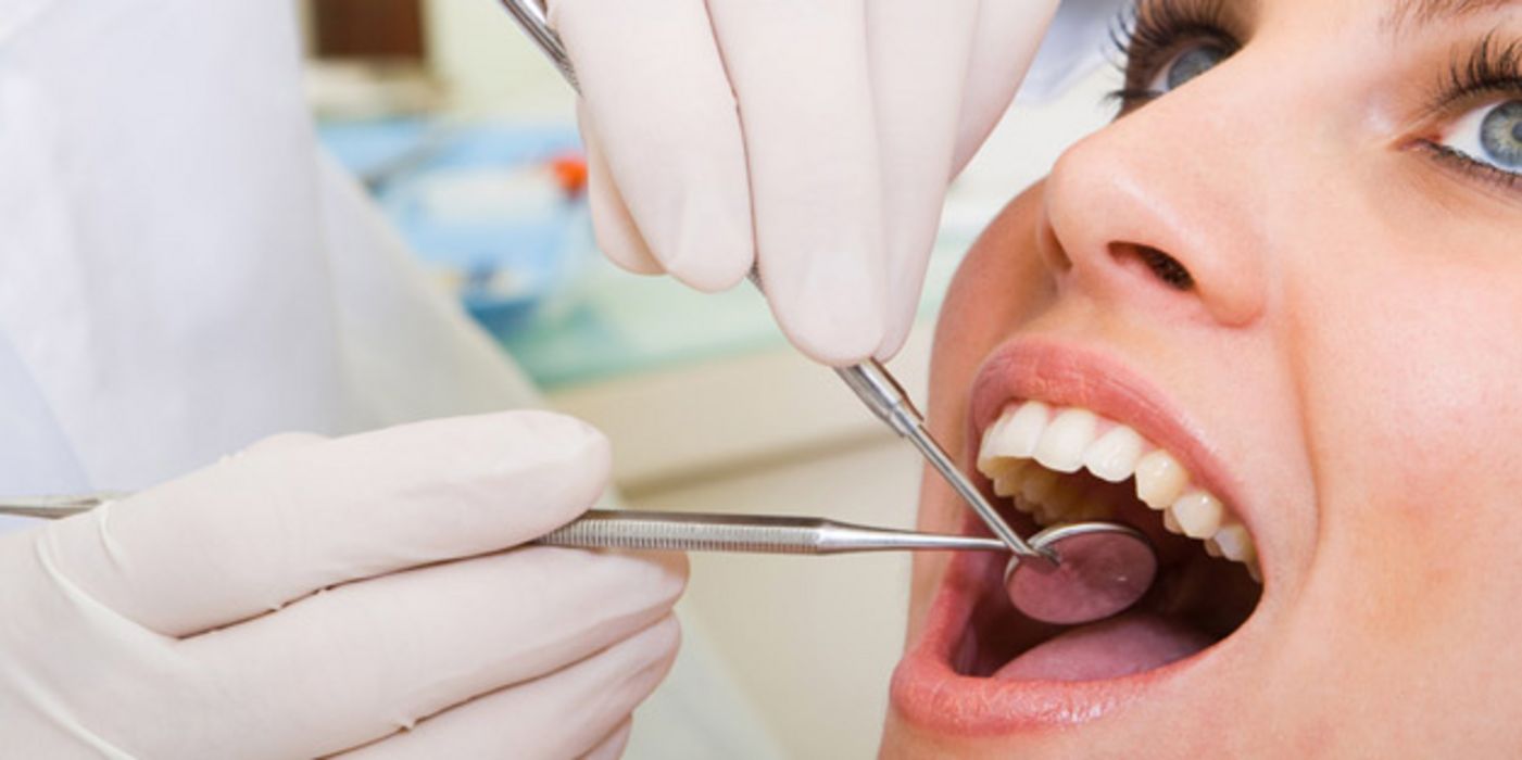 Junge Frau mit geöffnetem Mund beim Zahnarzt; vor dem Mund: Behandschuhte Hand hält Untersuchungswerkzeug