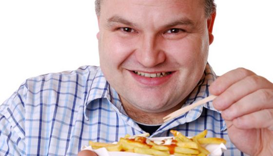 Übergewichtiger Mann ca. Ende 30 in blaukariertem Hemd (Brustbild) lacht in die Kamera, in der Hand ein Schälchen mit Pommes