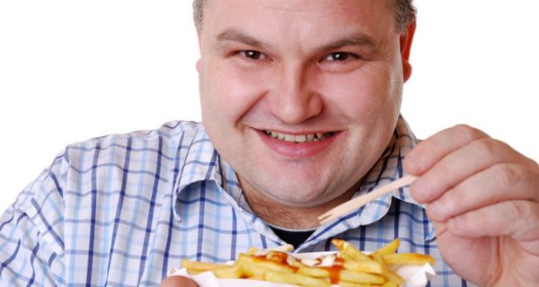 Übergewichtiger Mann ca. Ende 30 in blaukariertem Hemd (Brustbild) lacht in die Kamera, in der Hand ein Schälchen mit Pommes