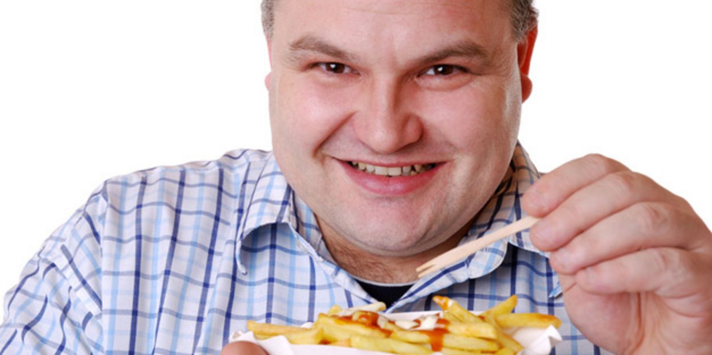 Übergewichtiger Mann ca. Ende 30 in blaukariertem Hemd (Brustbild) lacht in die Kamera, in der Hand ein Schälchen mit Pommes