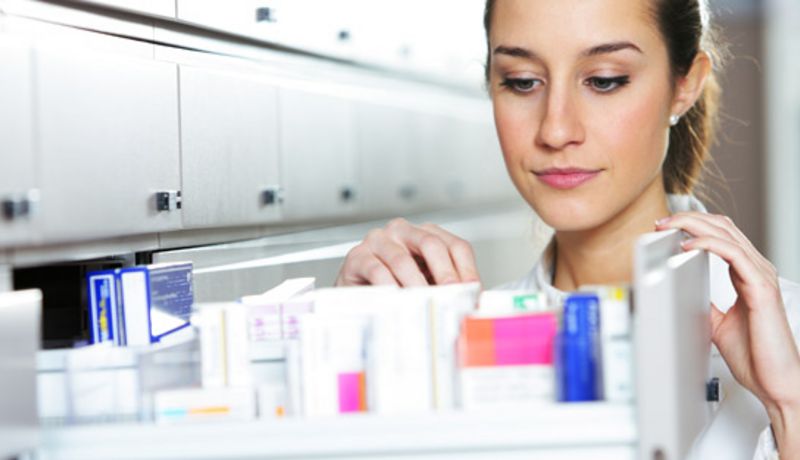 Apothekerin steht vor einem geöffneten Medikamentenschrank.