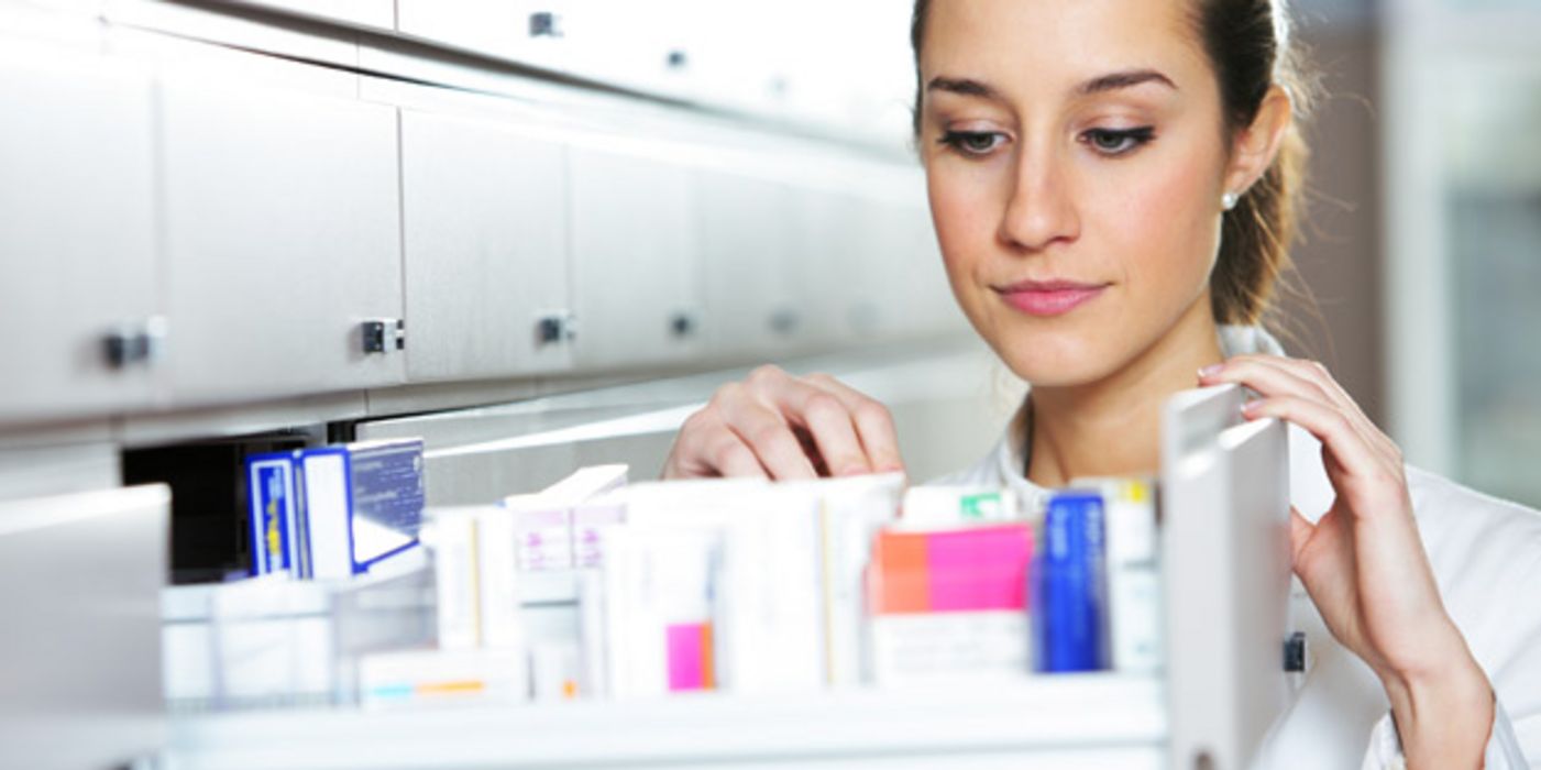 Apothekerin steht vor einem geöffneten Medikamentenschrank.