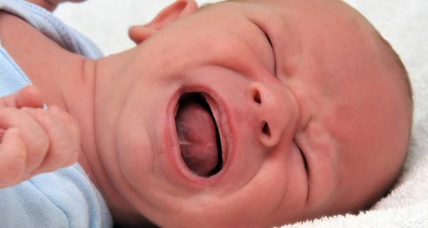 Säugling in blauem Strampler schreit vor Schmerz
